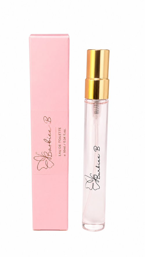 A clear glass perfume spray vial with a shiny gold atomizer cap stands next to its light pink rectangular box. Both pieces feature the 'Barbie B' logo and flower graphic printed in black and gold, set against a plain white background.